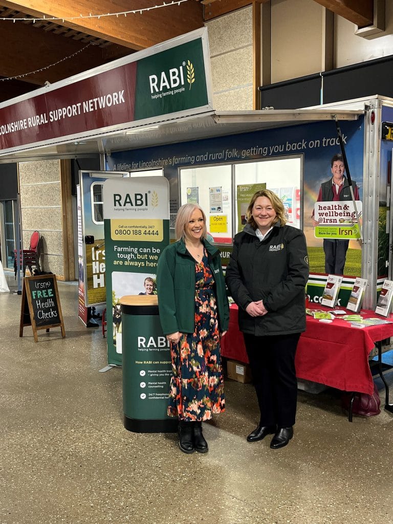 Two LRSN team members standing at an RABI stand with the LRSN Health Hut behind them