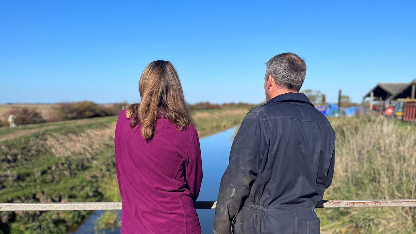Two people standing on a bridge over a dyke